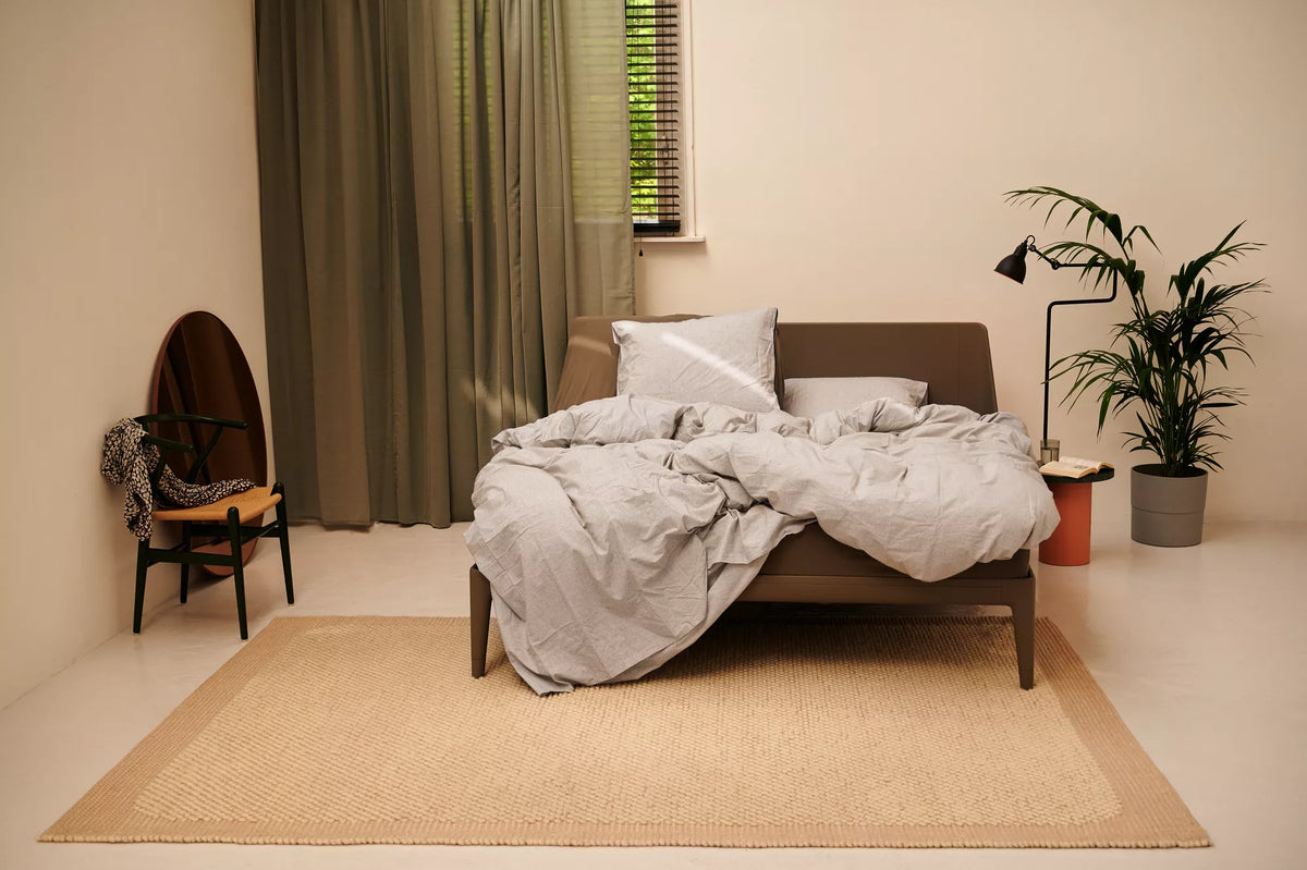 Auping Essential bed in de kleur Warm Grey met opgemaakt beddengoed in een warme, lichte slaapkamer